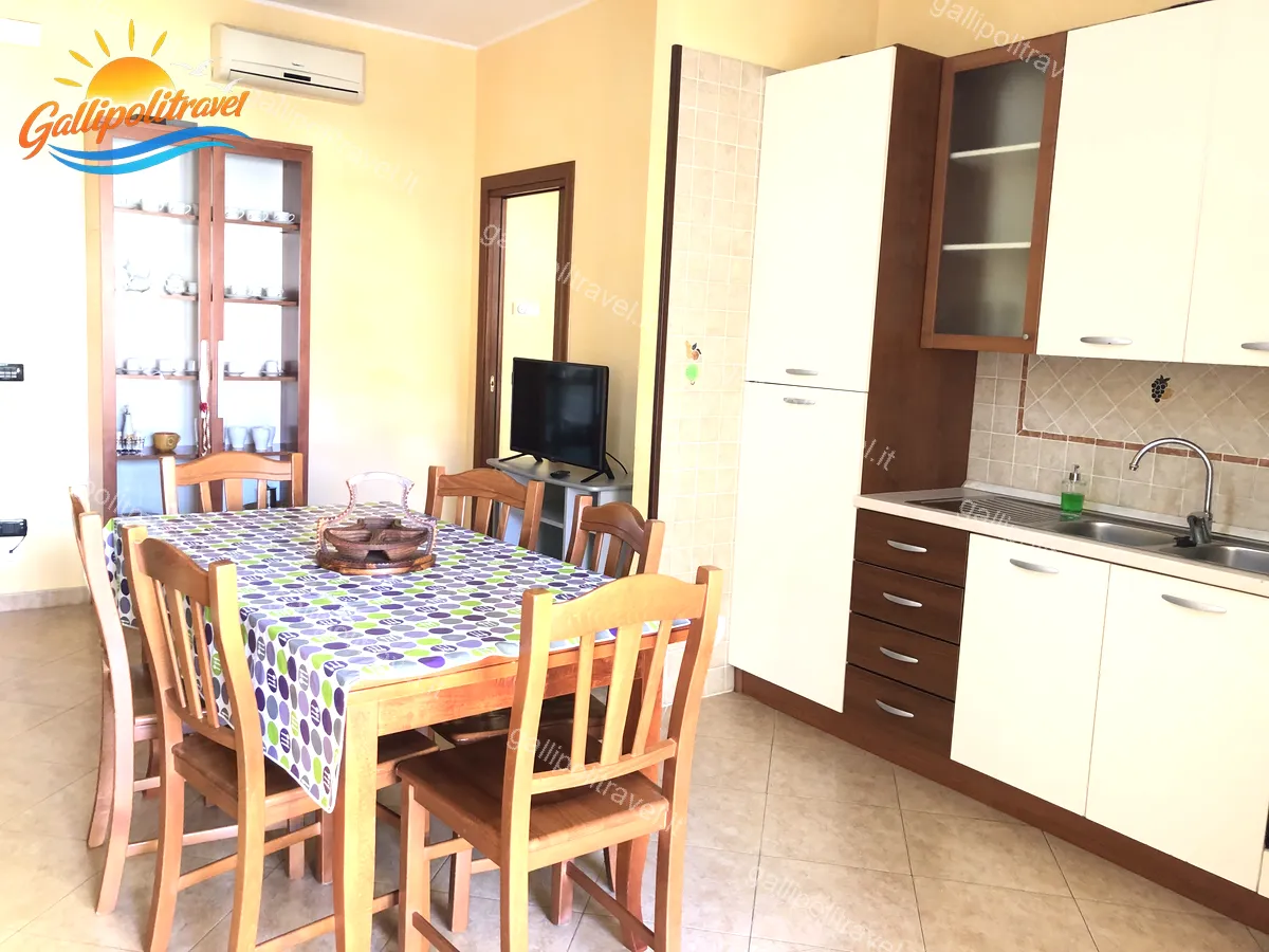 Wohnzimmer mit Holz-Sideboard, weißer Küche und Fernseher der Dreizimmerwohnung D1/3 Gallipoli