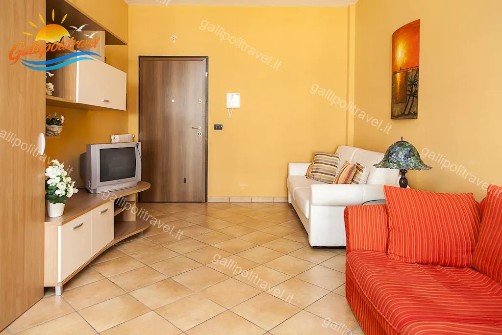 Wohnzimmer mit Bücherregal, Fernseher und rotem Sofa der Dreizimmerwohnung F1/1, Rosa Virginia