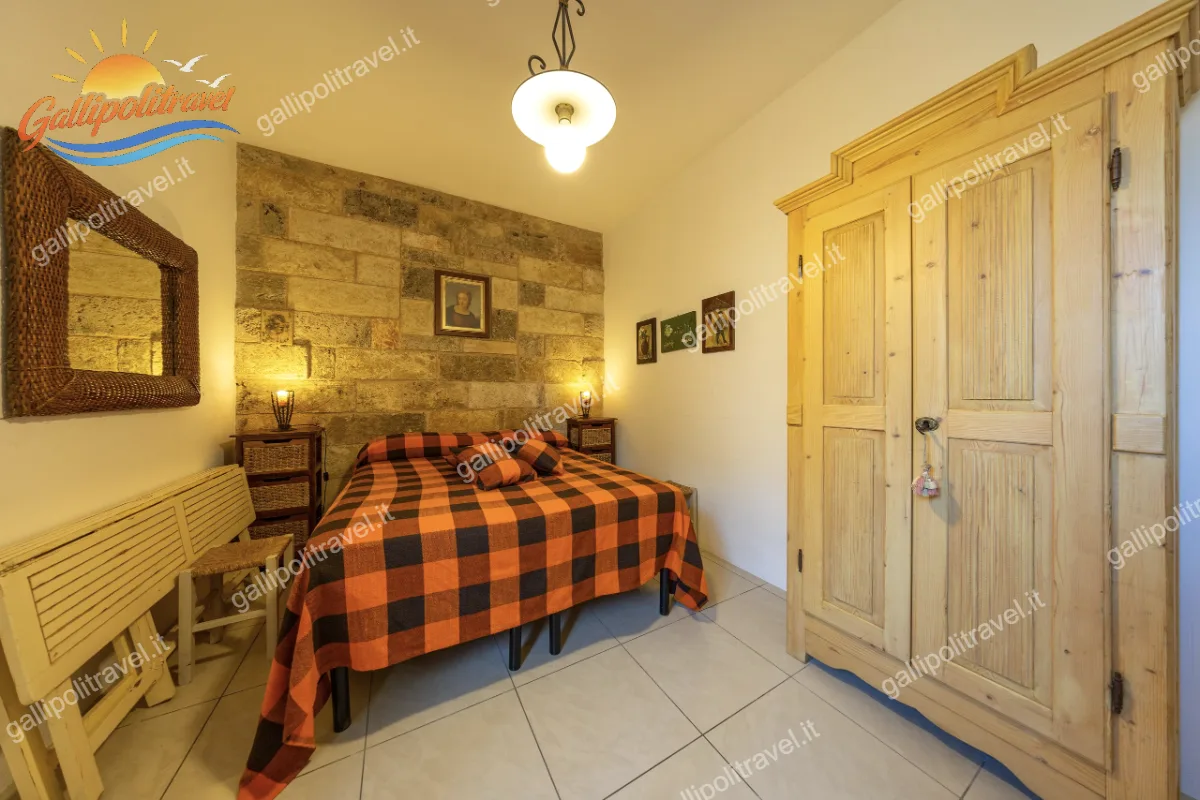 Camera da letto matrimoniale dal fascino rustico, illuminata da luci calde, con parete in pietra, copriletto a scacchi arancioni e neri e un grande armadio in legno massello