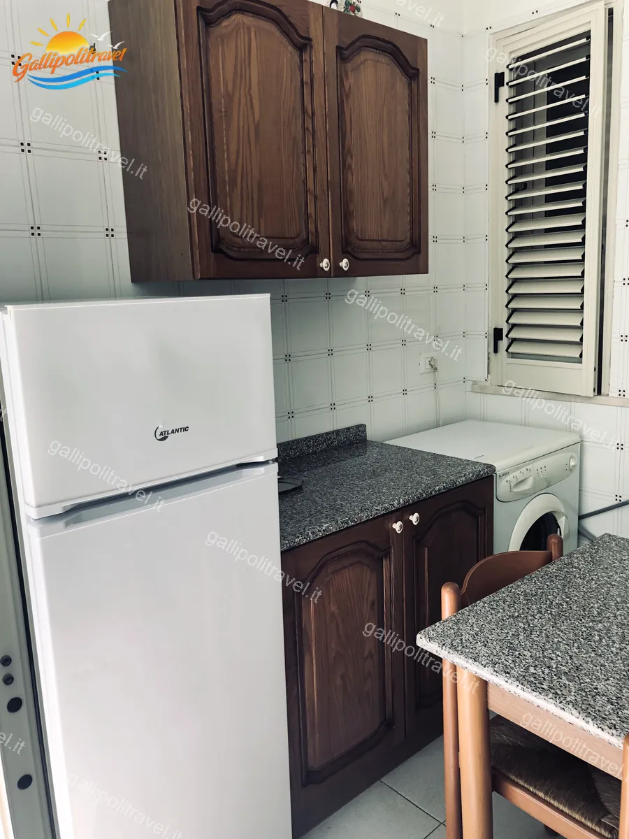 Cuisine avec réfrigérateur, lave-linge et armoires en bois de l'appartement trois pièces Tamerici 02, Baia Verde Gallipoli